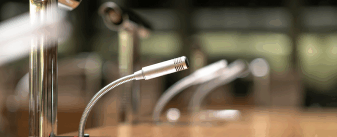 Close-up of a conference table microphone with a blurred background of additional microphones in a meeting room.