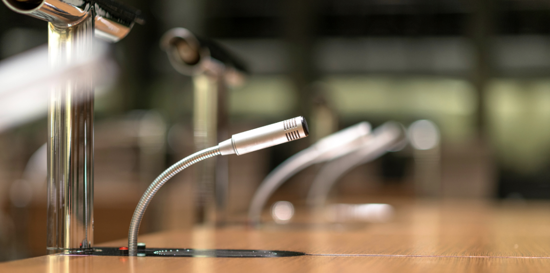 Close-up of a conference table microphone with a blurred background of additional microphones in a meeting room.