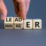 Manager versus leader symbol. Businessman flips wooden cubes and changes the word 'manager' to 'leader'. Beautiful grey background, copy space. Business and manager versus leader concept.