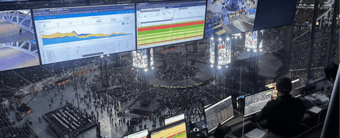 Control room view of a crowded arena event with a central stage, while staff monitor data dashboards and live feeds on multiple screens.